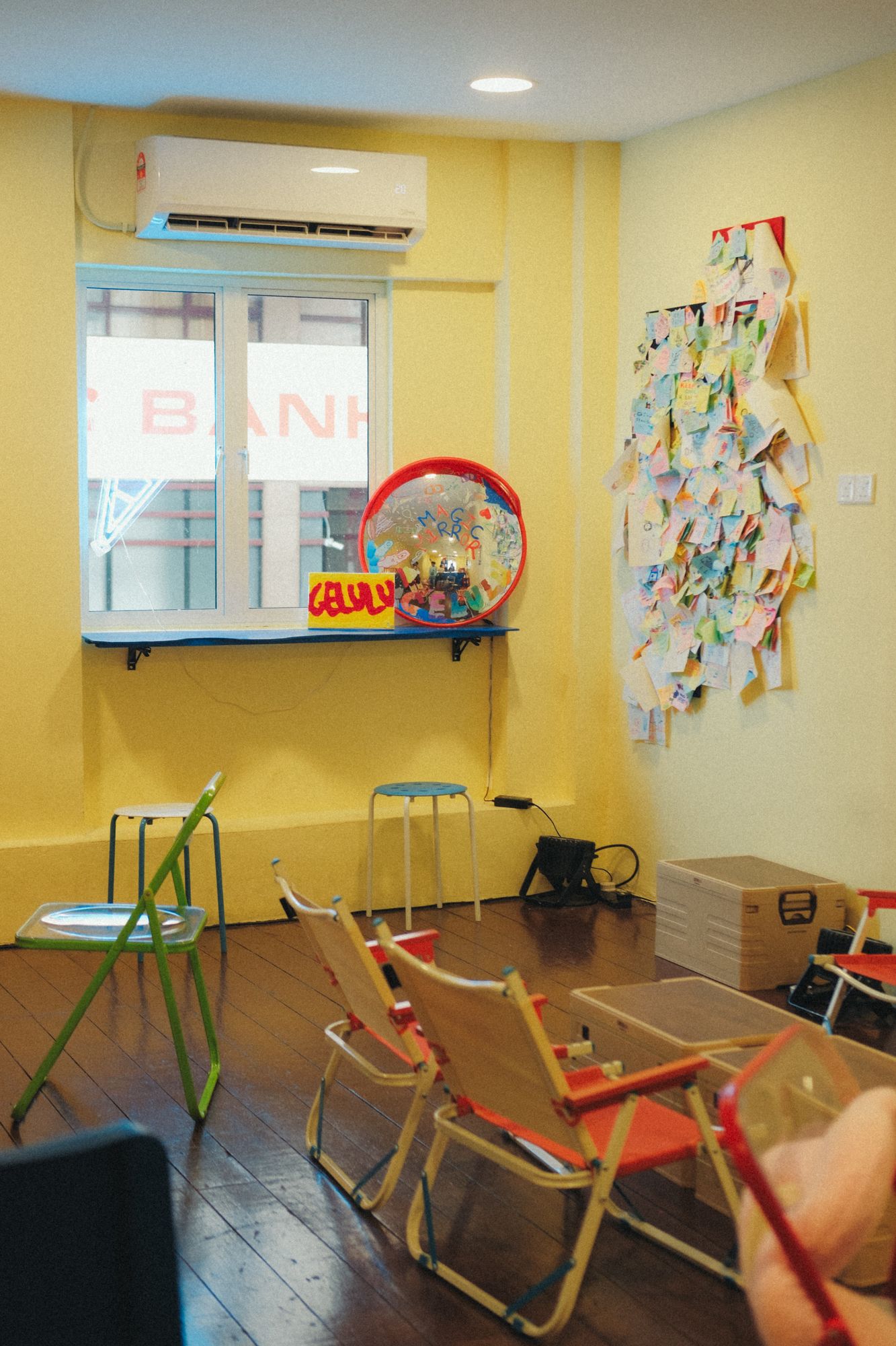 Inside the shop: yellow walls, folding chairs and the window over the street